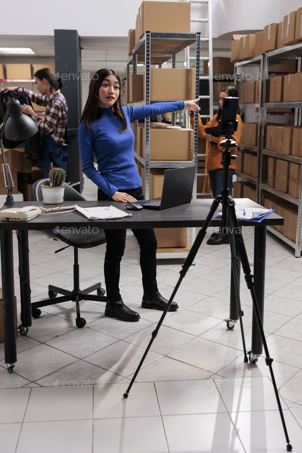 Asian woman recording employee testimonial video in industrial warehouse