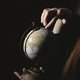  a young girl in a dark room holding a globe in her hands and looking for countries on it - PhotoDune Item for Sale