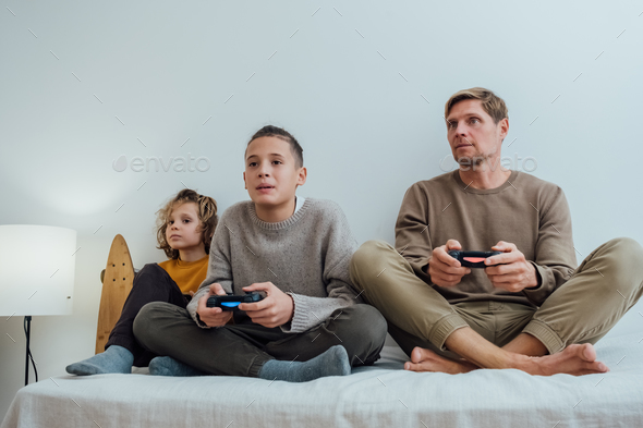 Father and children boys with joysticks playing video games at home - Stock Photo - Images