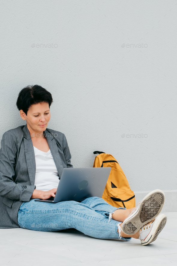Woman sitting with her back to wall works with computer Urban lifestyle portrait - Stock Photo - Images