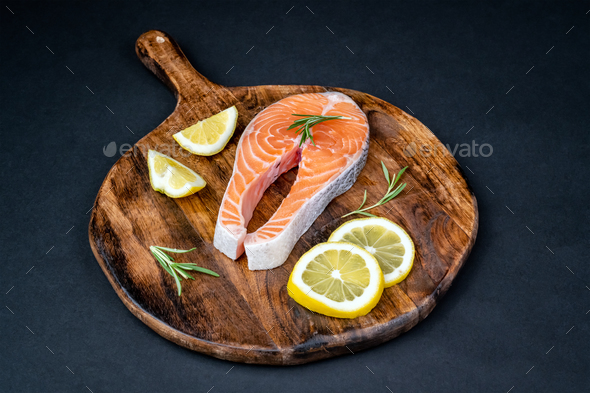 Fresh raw salmon slice with lemon and rosemary on a wooden board - Stock Photo - Images