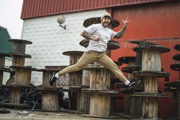 Crazy Spanish guy wearing stylish clothes cheerfully jumping on background of industrial spools