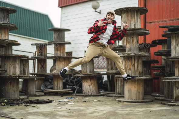 Crazy Spanish guy wearing stylish clothes cheerfully jumping on background of industrial spools
