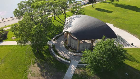 Drone view of park shelter with curved roof and open stage in park in midwest on a sunny day.