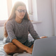young beautiful woman wearing glasses and gray dress working with laptop at home in bedroom - PhotoDune Item for Sale