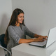 young beautiful woman wearing casual  gray dress working with laptop against white wall - PhotoDune Item for Sale