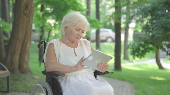 Positive Handicapped Senior Woman Messaging Online Outdoors. Portrait of Beautiful Paralyzed alt