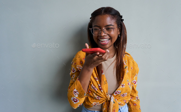 Isolated young woman on grey background using smartphone sending voice mails and smiling.