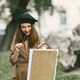 Girl in dress and black hat painting on an easel in a park - PhotoDune Item for Sale