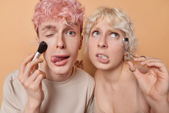 Photo of young woman and man use cosmetic brush and eyelash curller wink eye and stick out tongue
