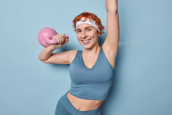 Motivated athletic redhead woman lifts weight works out in gym or at home being full of energy gets