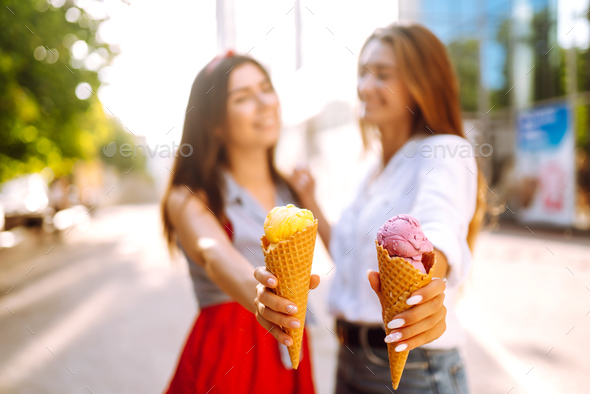 Ice cream in hands of beautiful young girls. Two female friends eat ice cream walking in the park.