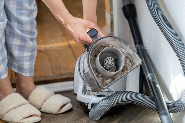 Female opening dust filter out of vacuum cleaner at home, hoover container full of dirt, pet hair