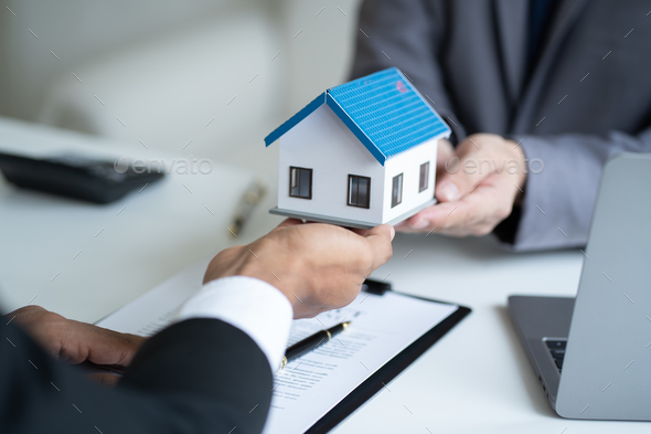 Close up view of real estate agent, and insurance salesman handing over a sample house to a client