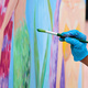 Artist&#39;s hand in blue gloves with paintbrush painting colorful picture at outdoor art festival - PhotoDune Item for Sale