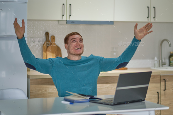 man at home laughing using laptop online, lucky winners. successful young man holding the computer