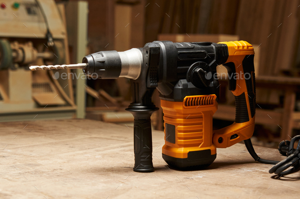 focus on the handle and vertical motor of the electric rotary hammer standing on a wooden table