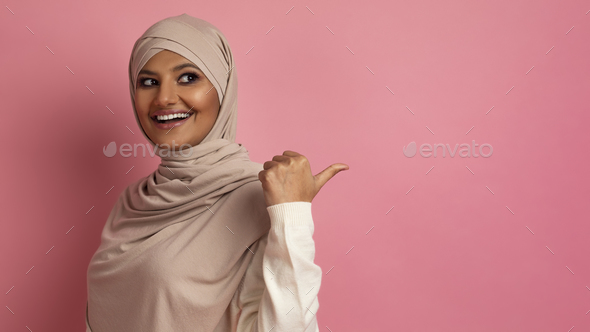 Happy Muslim Woman In Hijab Pointing At Copy Space Behind Her Back