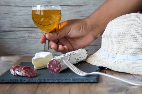 Man holding a glass of beer with brie cheese and smoked sausage on a board