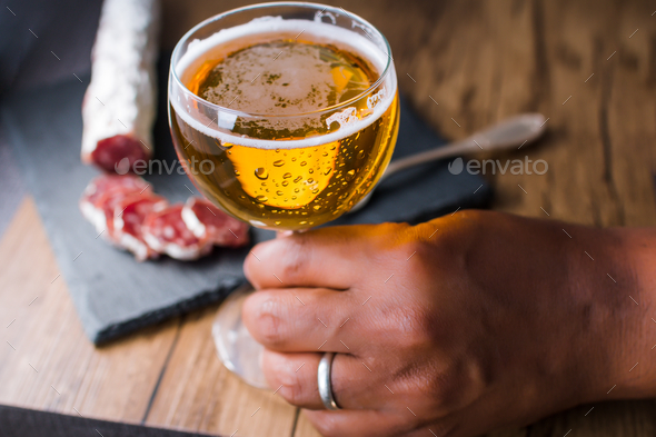 Man holding a glass of beer with brie cheese and smoked sausage on a board