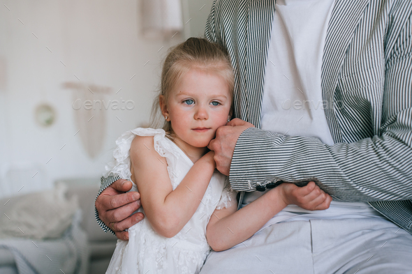 Cropped shoot of father calming little blonde daughter frustrated, needs more attention. Sad girl