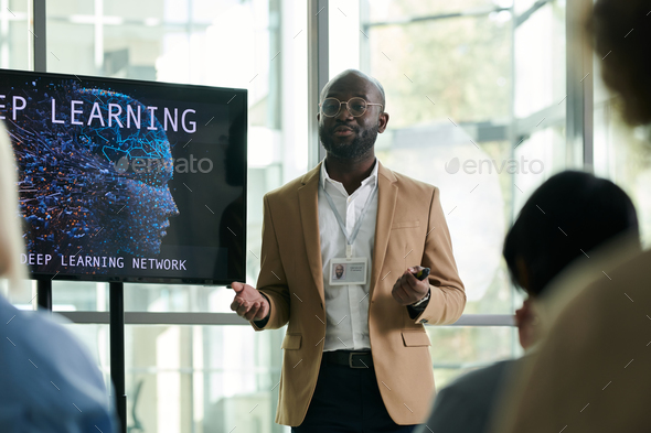 Young black man in formalwear standing by interactive board during presentation