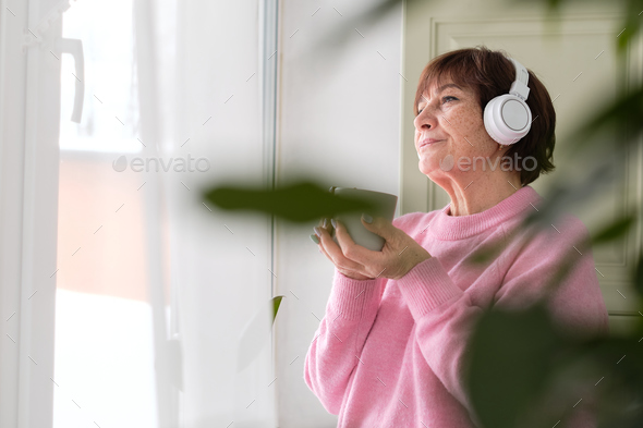 old lady with headphones, enjoying her coffee and music. technology can enhance the quality of life