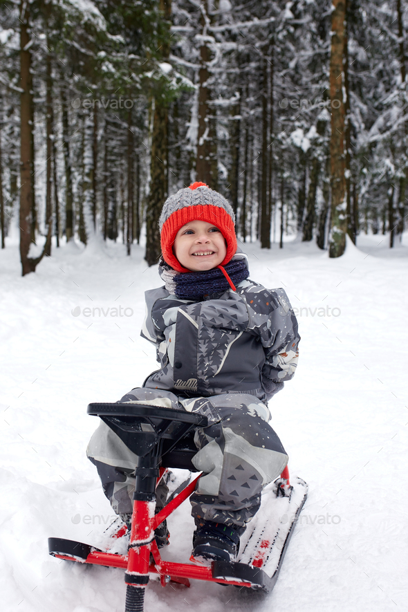 happy boy downhill on a sled in winter. a child in bright clothes sits on a  sled, snow is flying at Stock Photo by Gerain0812