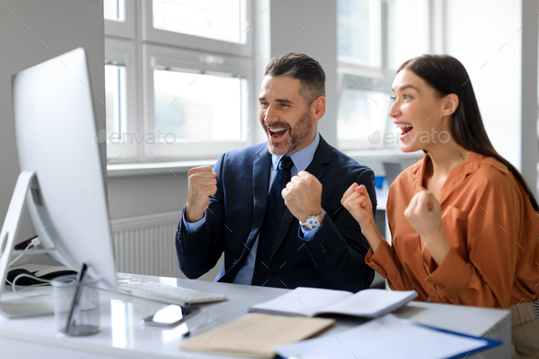 Overjoyed colleagues celebrating win, looking at computer screen and shaking fists, received good