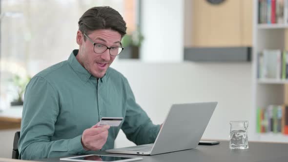 Middle Aged Man Excited By Online Shopping Success on Laptop alt