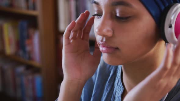 Asian female student wearing a blue hijab sitting and listening to music at library alt