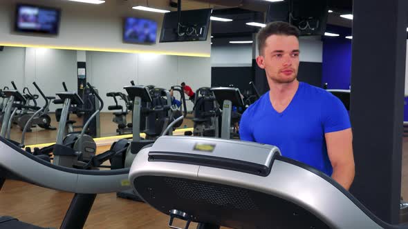 A Young Fit Man Walks on a Treadmill in a Gym - Closeup alt