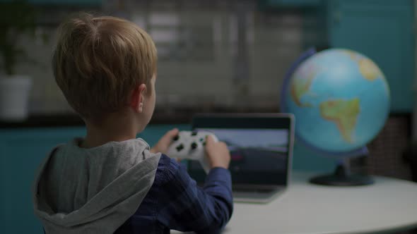 School Boy Playing Racing Video Game Holding Game Controller in Hands Sitting at the Table alt