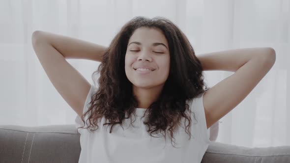 Happy African American Young Woman Sit Relax on Cozy Couch Hands Over Head Happy to Move to New alt