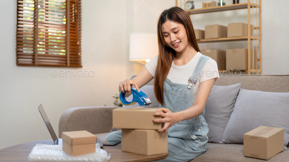 Young entrepreneur is packing clothes into cardboard boxes and using tape to seal for home delivery