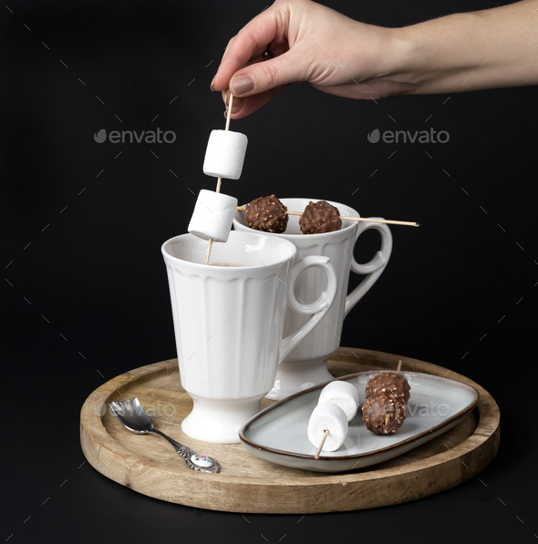 A woman's hand stirs hot chocolate with marshmallows and chocolates skewers - Stock Photo - Images