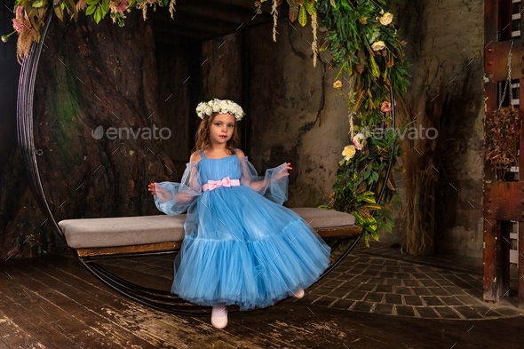 Little girl princess with blue eyes sits on fairy swing in dark mystery room
