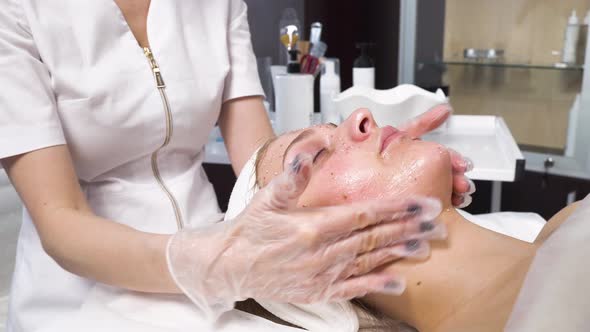 Cosmetologist a Woman Applies a Cosmetic Mask with Her Hands and Does a Massage