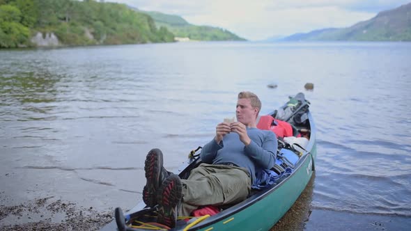 A Young Man Eating While Resting In A Boat On The River Of Caledonian Canal, Scotland - Close Up Sho alt