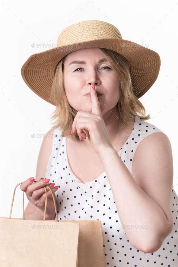 Female shopper raised finger to lips, makes secret sign, holds paper shopping bag in her other hand
