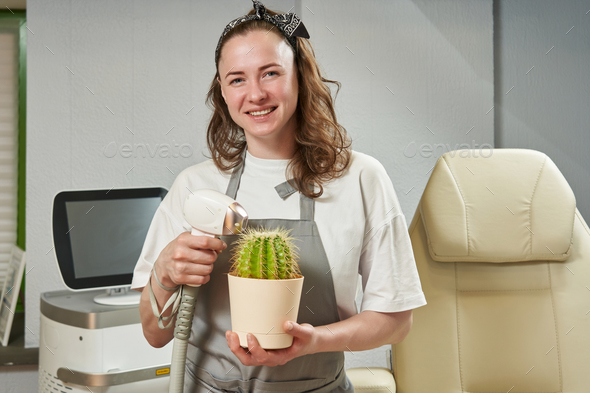a young beautiful woman, a hair removal master, holds a laser device in her hands next to a cactus