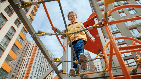 Little smiling boy crossing rope bridge between two towers on outdoor kids  playground Stock Photo by kryzhov