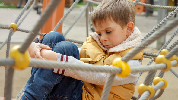 Sad lonely boy having no friends sitting on playground alone. Child depression