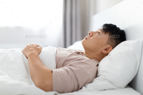 Frustrated asian man lying in bed in the morning