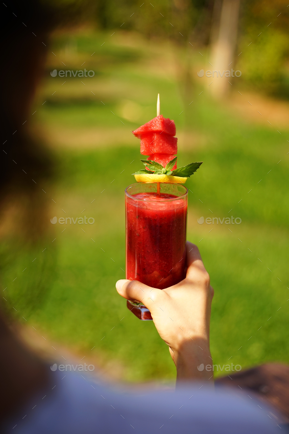 Vertical shot of a person holding a glass of watermelon shake with lemon and mint in a garden