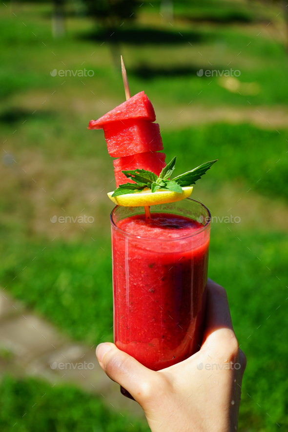 Vertical shot of a person holding a glass of watermelon shake with lemon and mint in a garden