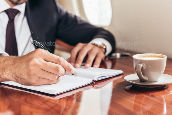 cropped view of businessman writing in notebook in private plane