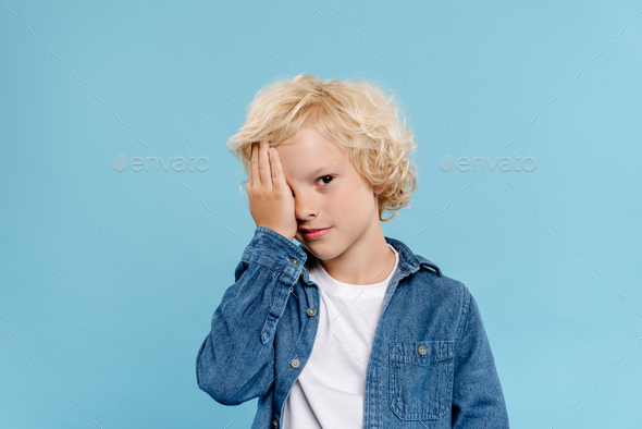 tired and cute kid obscuring face isolated on blue