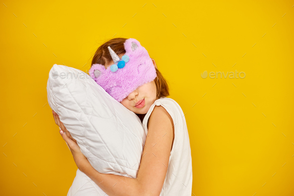 Nice teenage girl in white pyjamas with a violet sleeping mask embraces a pillow - Stock Photo - Images