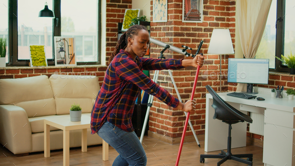 Cheerful girlfriend dancing in apartment and using mop to sweep floors